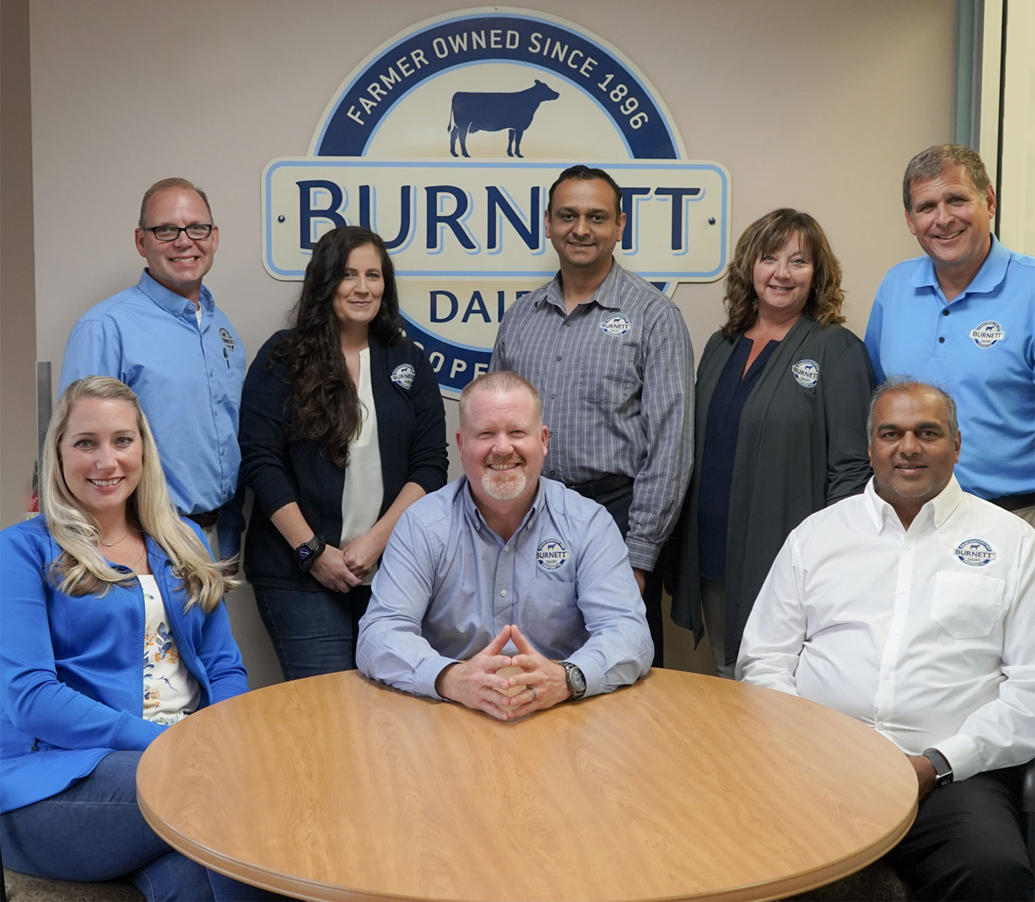 Burnett Dairy Leadership Team surrounding a table and logo on the wall behind